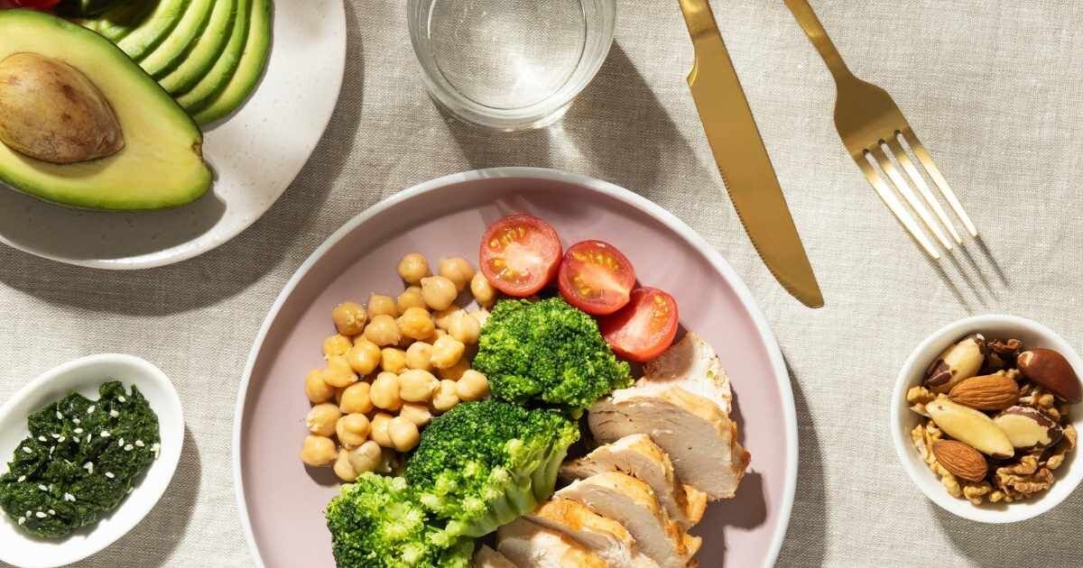 A healthy keto meal featuring chicken, broccoli, chickpeas, and avocado with nuts on the side.